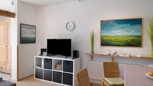 A living room with a television, a clock, a painting, and a radiator.