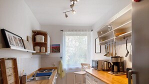A kitchen with a wooden countertop, white cabinets, a coffee maker, and a window with a view of trees.