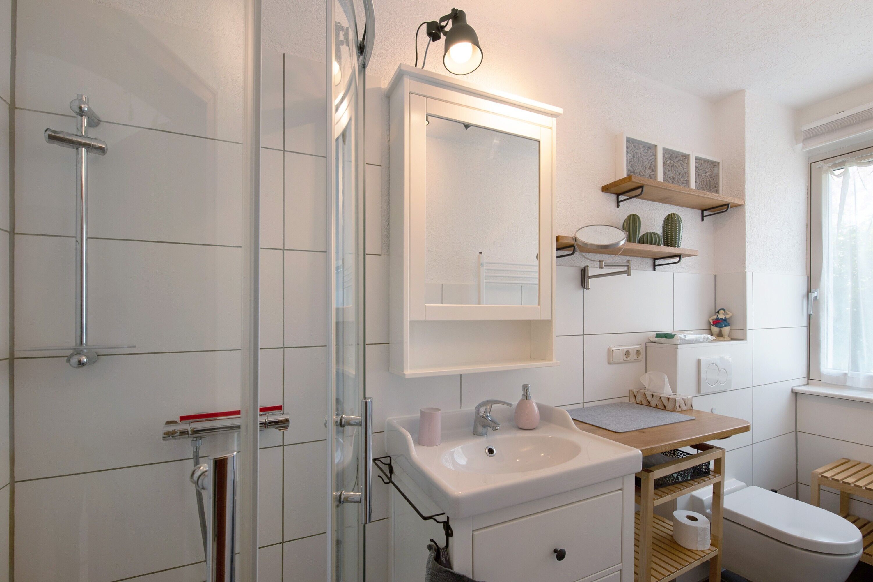 Une salle de bain équipée d’une douche, d’un lavabo, de toilettes et d’un miroir avec des étagères au-dessus.