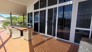 A covered patio with a table and chairs, large sliding glass doors, and a view of the surrounding area. - BankSea Holiday Home (Agnes Water)