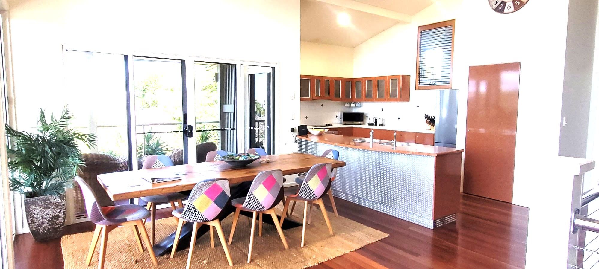 A dining area with a wooden table and chairs, a kitchen with wooden cabinets, and a large window.