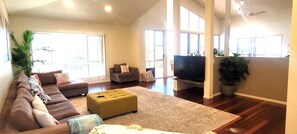 A spacious living room with a large sofa, ottoman, and a flat-screen TV. - BankSea Holiday Home (Agnes Water)