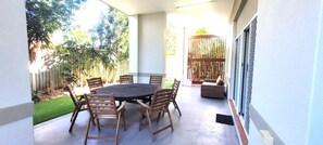 A covered patio with a round table and chairs, surrounded by a wooden fence and a small garden. - BankSea Holiday Home (Agnes Water)