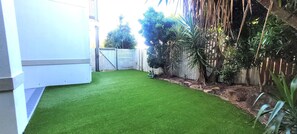 A small, enclosed garden area with artificial grass, a wooden fence, and various plants. - BankSea Holiday Home (Agnes Water)