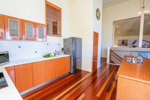 A kitchen with wooden cabinets, a refrigerator, a microwave, and a sink. - BankSea Holiday Home (Agnes Water)