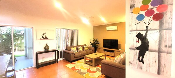 A living room with a sofa, coffee table, TV, and a painting on the wall. - BankSea Holiday Home (Agnes Water)