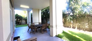 A covered patio with a table and chairs, a wooden fence, and a lawn. - BankSea Holiday Home (Agnes Water)