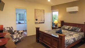A bedroom with a wooden bed, a chair, a bedside table, and a window with a view. - BankSea Holiday Home (Agnes Water)
