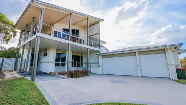 A two-story house with a balcony, a garage, and a well-maintained lawn. - BankSea Holiday Home (Agnes Water)