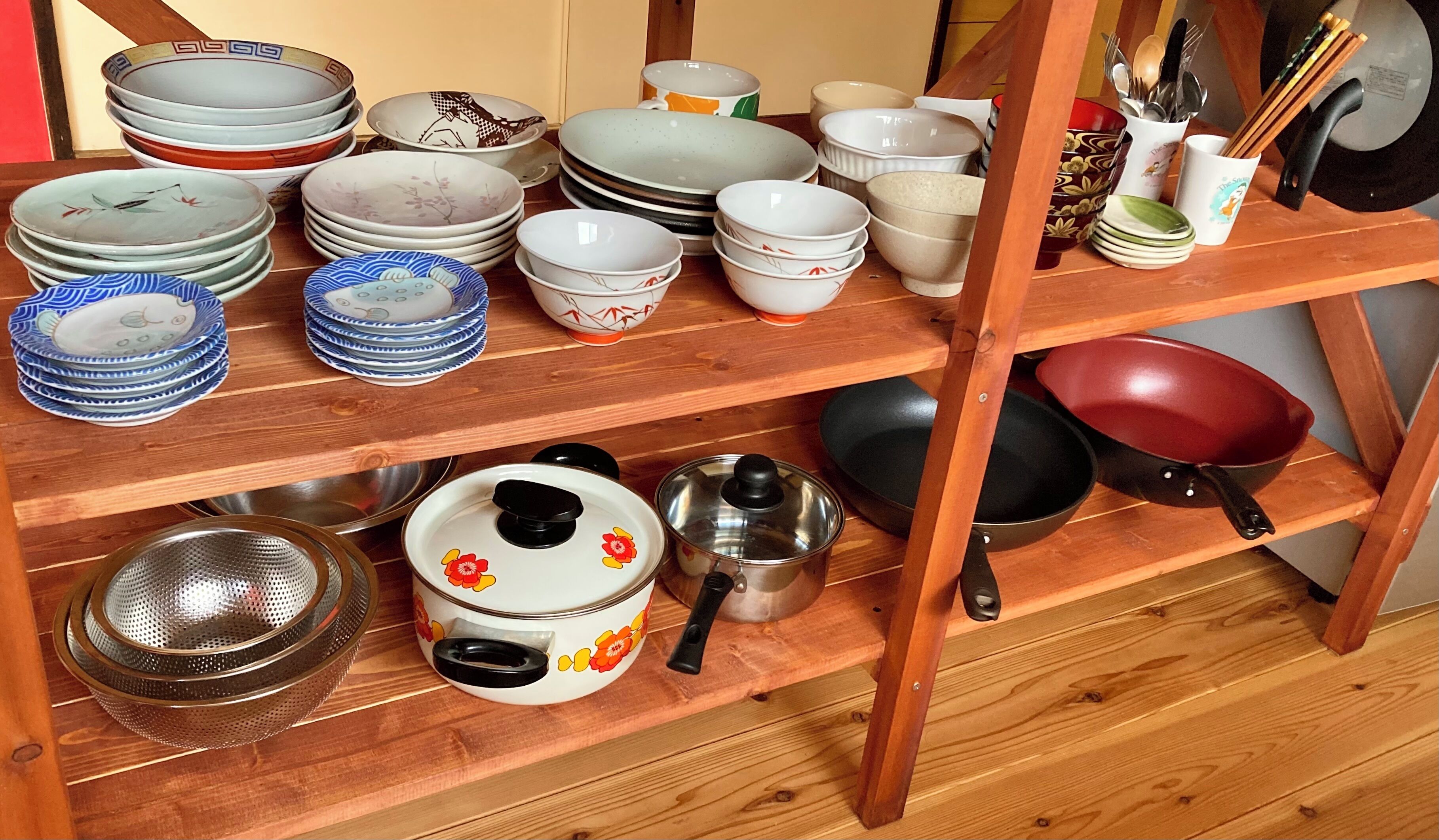 Uma prateleira de madeira com diversos utensílios de cozinha, incluindo pratos, tigelas, um escorredor e uma frigideira.
