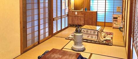A traditional Japanese room with tatami flooring, a low table, a heater, and a futon bed.