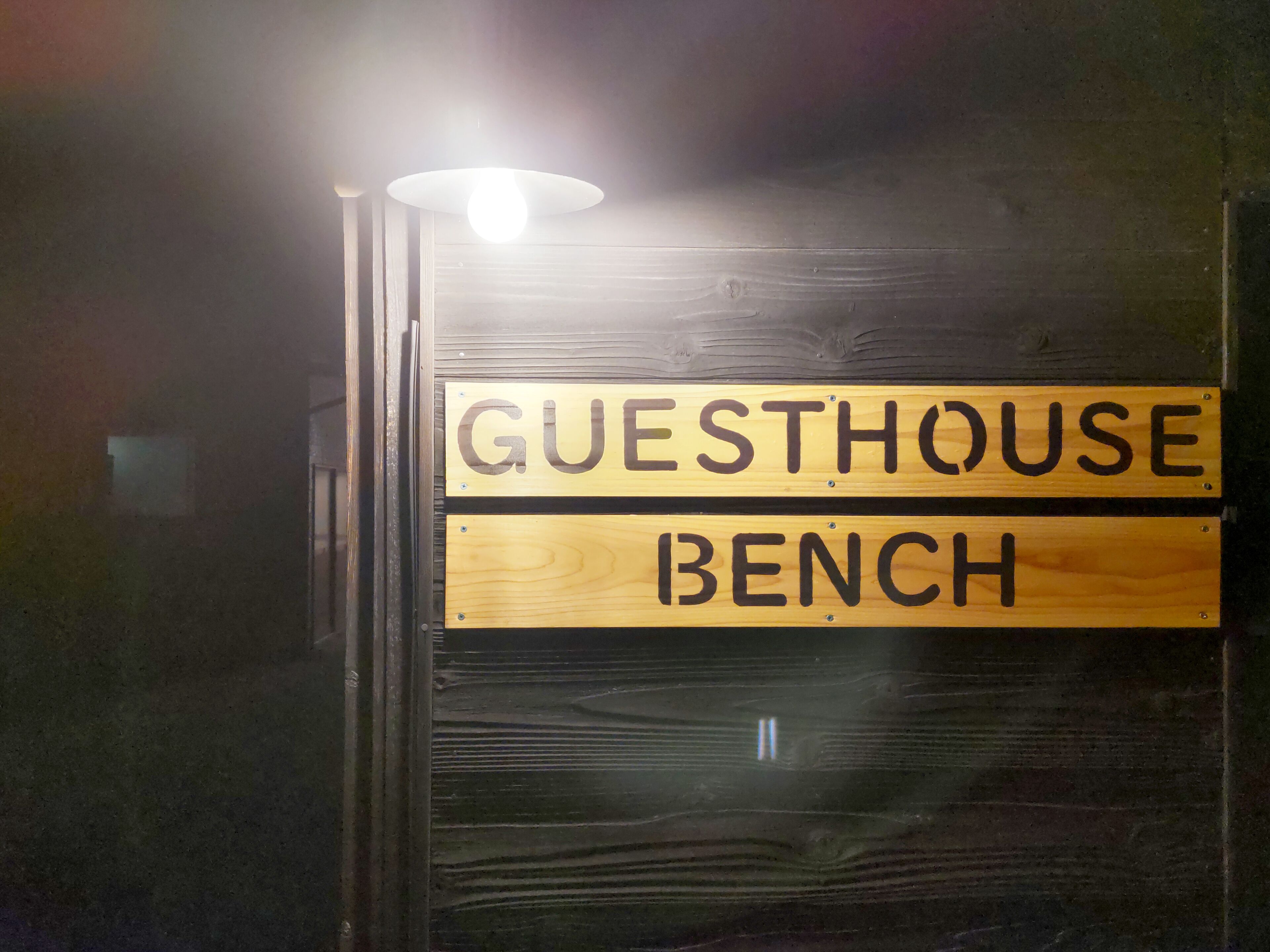 Un cartello di legno con la scritta 'GUESTHOUSE BENCH' che indica una zona riservata agli ospiti.
