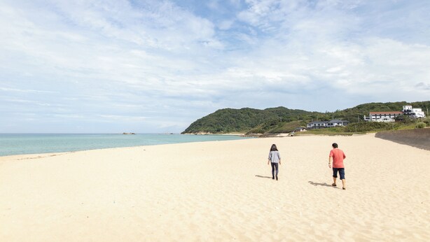 Ein weiter Sandstrand mit blauem Himmel und hügeliger Landschaft im Hintergrund.