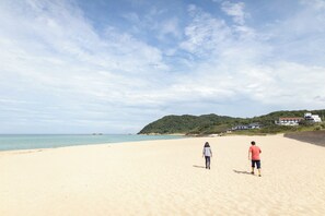 Une vaste plage de sable fin, un ciel dégagé et un paysage vallonné en arrière-plan.