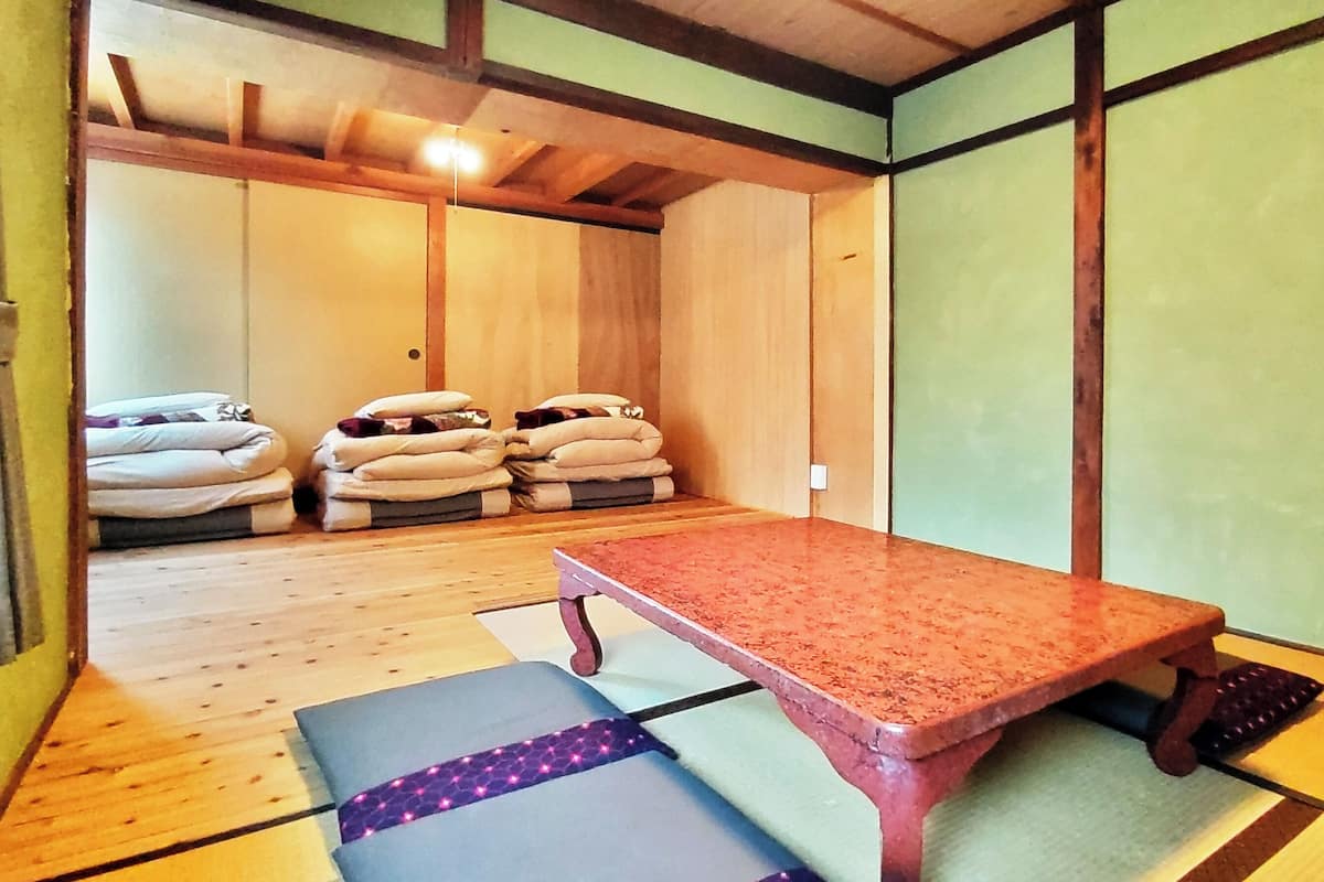 Una habitación con tatamis, una mesa de madera, cojines y techo de madera.