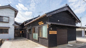 Ein traditionelles japanisches Gästehaus mit Holzbeschichtung, einem Schild, das auf ein Gästehaus hinweist, und blauem Himmel.