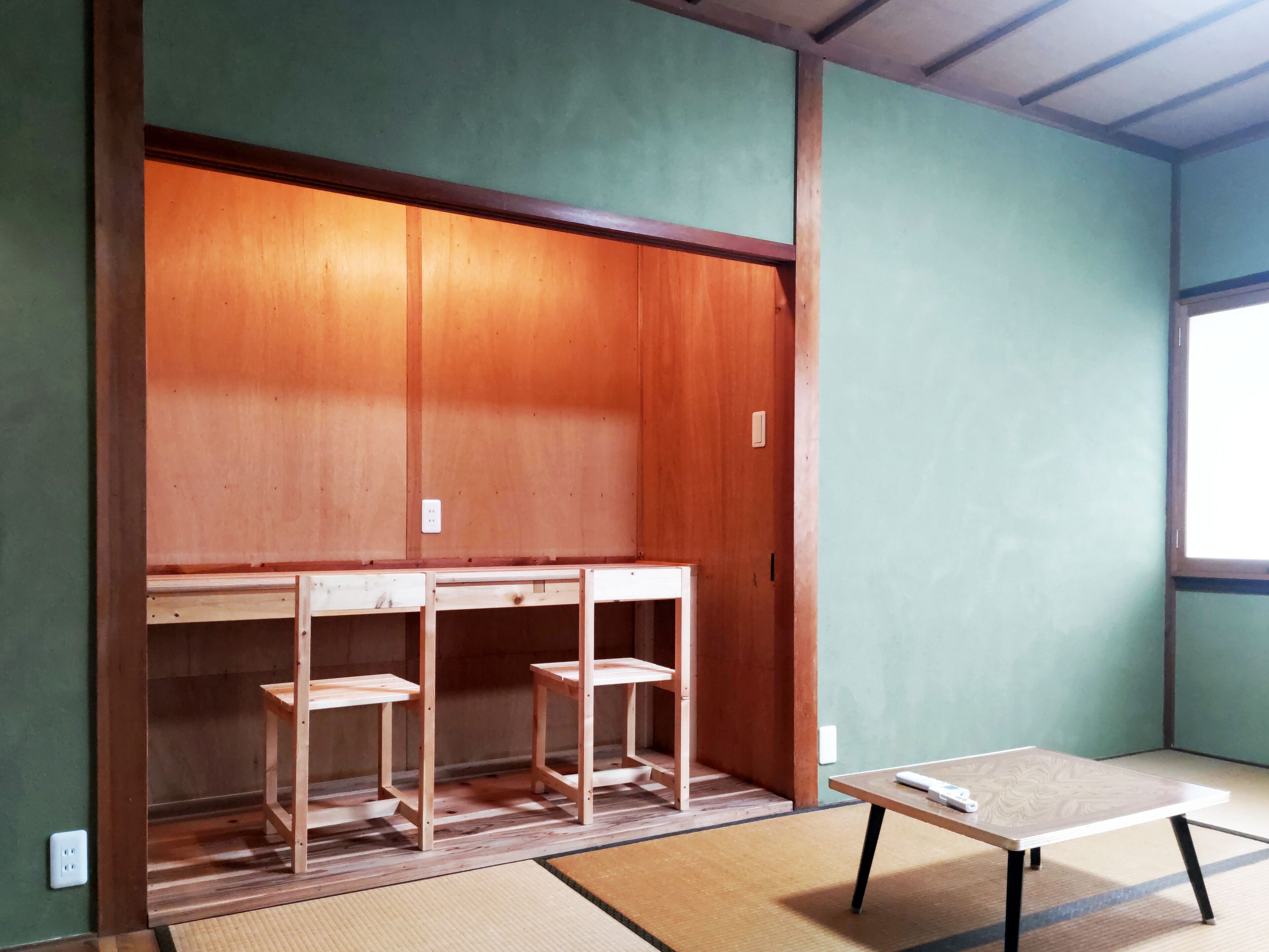 Une pièce avec une armoire en bois, un sol recouvert de tatamis et une petite table avec une télécommande.