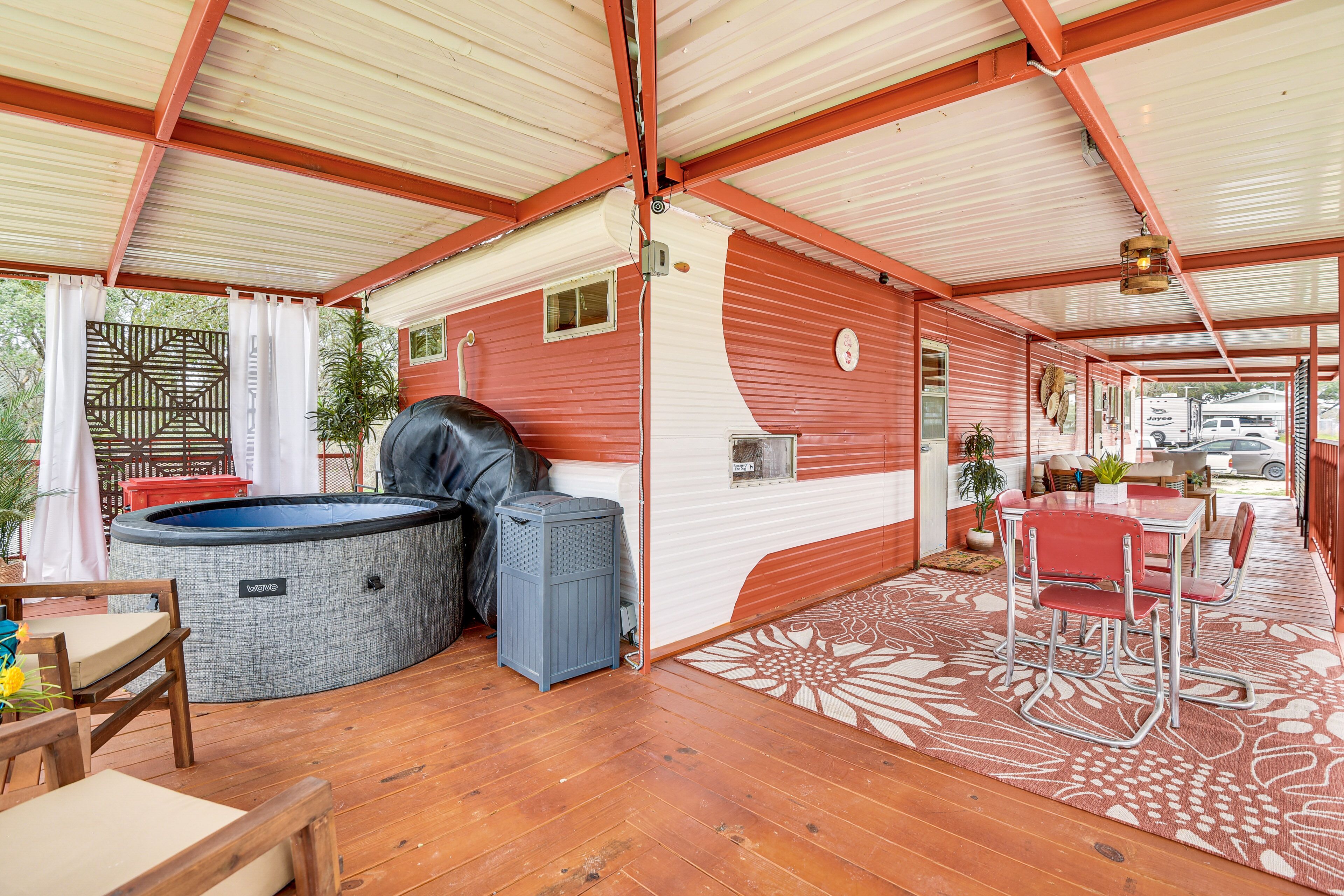 A covered outdoor area with a hot tub, seating, and a patterned rug.