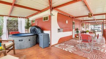 A covered outdoor area with a hot tub, seating, and a patterned rug.