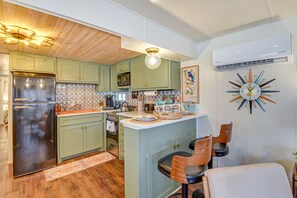 Una cocina con un refrigerador de acero inoxidable, un microondas y una estufa. El techo es de madera y hay un reloj en la pared.