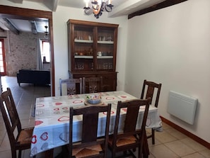 Un comedor con una mesa dispuesta para cuatro personas, rodeada de sillas de madera. Se observa un aparador de madera con puertas de cristal al fondo.