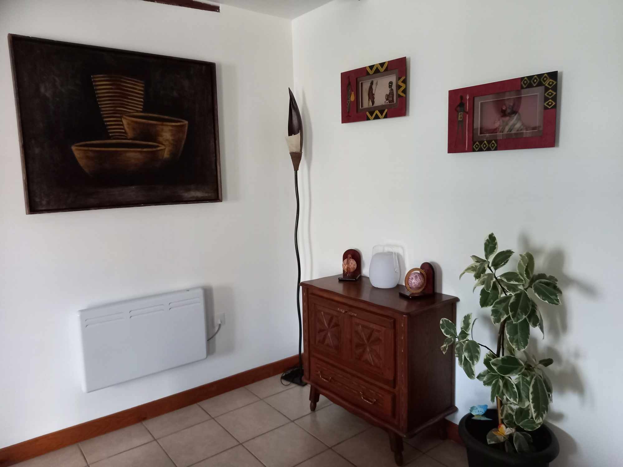 A room with a radiator, a wooden cabinet, a potted plant, and framed pictures on the wall.