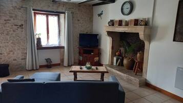 A living room with a sofa, a television, a fireplace, and a clock on the wall.