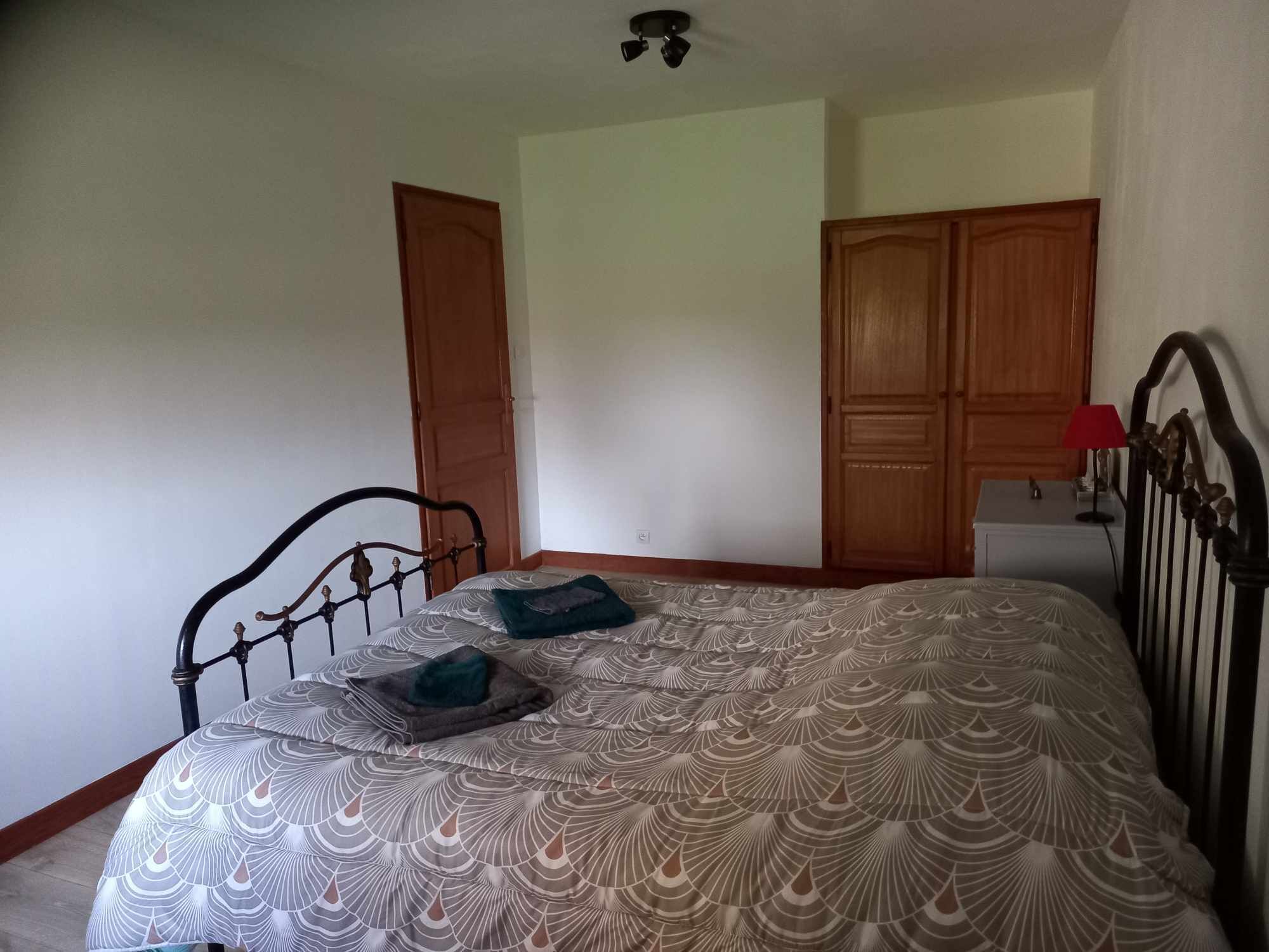 A bedroom with a bed, a nightstand, a lamp, and two wooden doors.