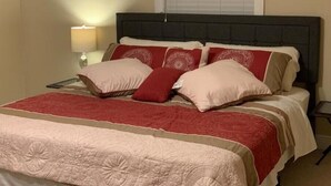 En pænt redt seng med et rødt og beige sengetæppe, en mørk sengegavl og en sengetøjslampe.
