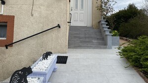 Una casa de dos pisos con una puerta blanca, un pequeño porche de guijarros blancos y esculturas de animales negros, y un muro de ladrillo.