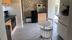 Una cocina compacta con pared de piedra, microondas, refrigerador negro, armarios de madera, mesa de mármol y una silla blanca.