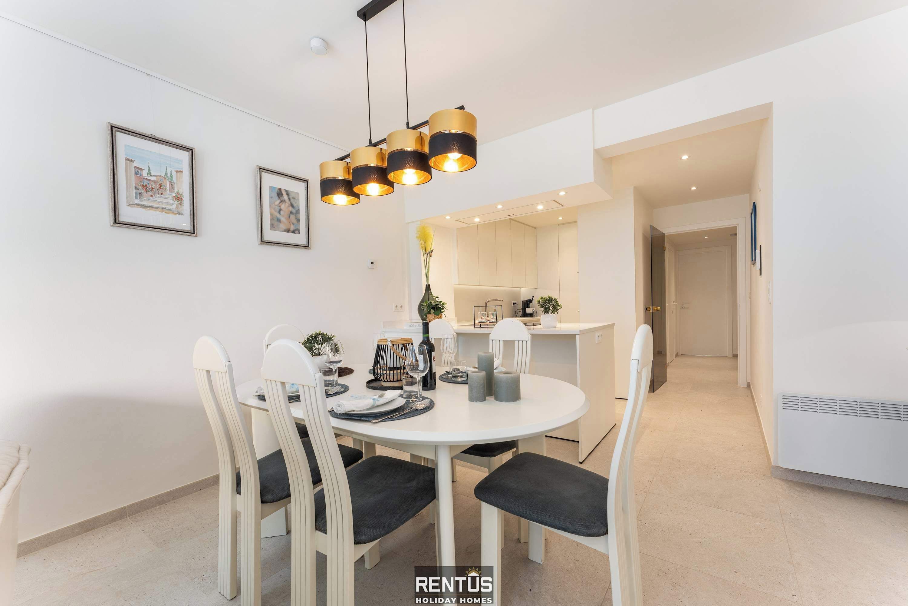 A modern dining area with a round table, white chairs, and a black and gold pendant light.