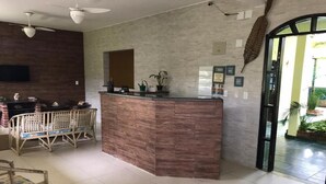 Un espace d’accueil avec un comptoir de réception en bois, un coin salon avec des fauteuils, un téléviseur à écran plat fixé au mur et un ventilateur de plafond.