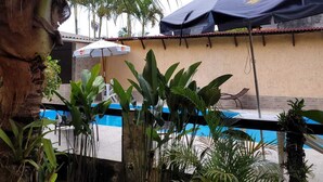 Un espace piscine avec une piscine bleue, entourée de plantes tropicales et d’un palmier.