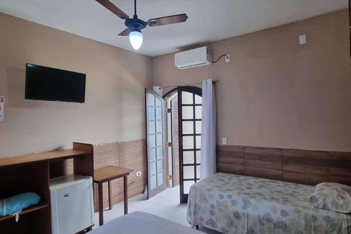 A bedroom with a bed, a desk, a chair, a ceiling fan, and an air conditioning unit.