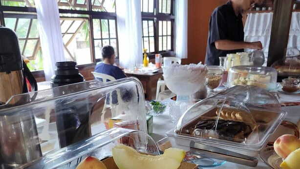 Un buffet proposant une variété de fruits et de desserts, notamment de la papaye et des pêches, dans une pièce dotée de grandes fenêtres et de murs en briques.