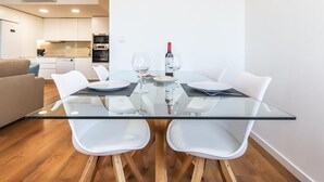 Un comedor moderno con una mesa de vidrio, sillas blancas y una cocina al fondo.