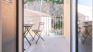 Un balcón con mesa y sillas, vista a una ladera rocosa y un edificio al fondo.