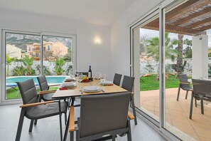Uma sala de jantar com mesa posta para quatro pessoas, grandes janelas e vista para uma piscina e edifícios.