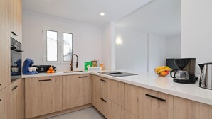 A modern kitchen with wooden cabinets, a white countertop, and various appliances including a coffee maker and a kettle. - Limoncello - Denia, Costa Blanca (Denia)