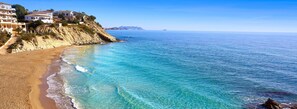 Une propriété située sur la côte, avec une plage, une eau d’un bleu cristallin et un paysage montagneux en arrière-plan.