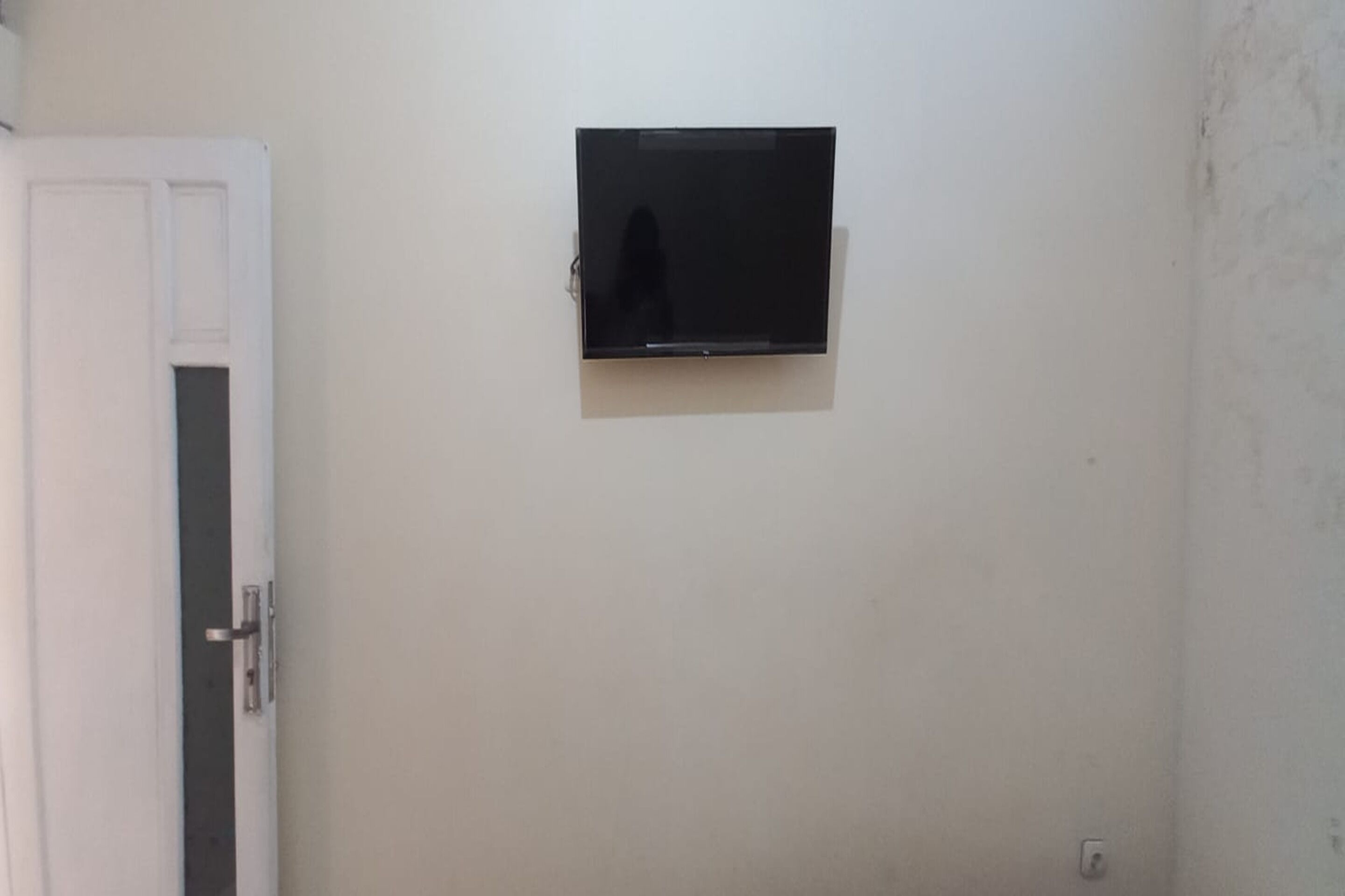 Una habitación con la puerta cerrada, un televisor instalado en la pared y un enchufe visible.
