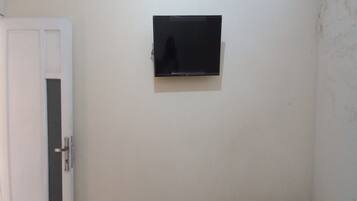 Una habitación con la puerta cerrada, un televisor instalado en la pared y un enchufe visible.