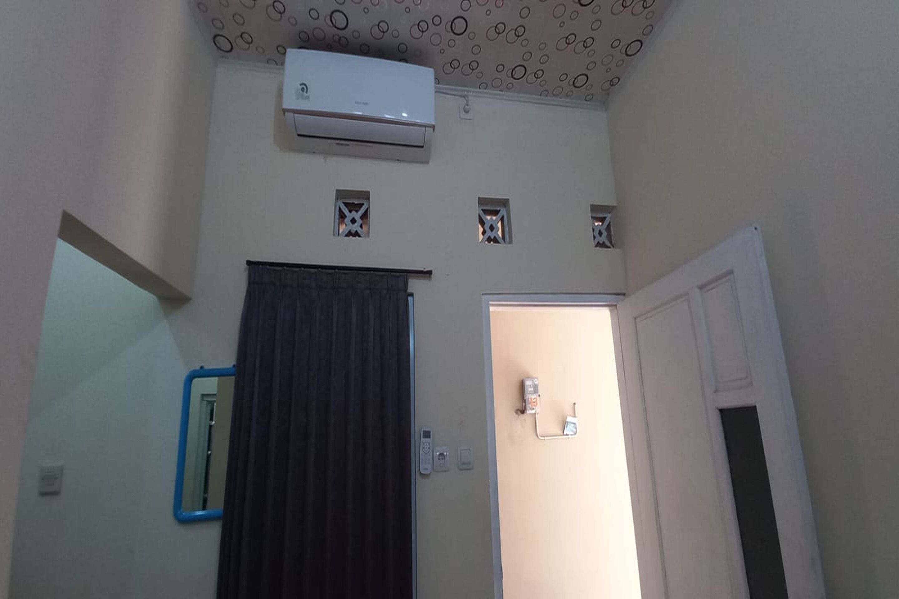 A room with a door, a mirror, a window, and an air conditioner on the wall.