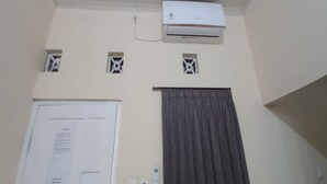 Ein Zimmer mit einer weißen Wandklimaanlage, einer Tür mit einem Korkbrett und einem Fenster mit Vorhang.