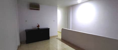 A hallway with a tiled floor, a black console table with a vase, and a wall-mounted air conditioner.