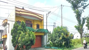 A two-story building with a red door and a balcony. There are trees in front of the building and a motorcycle on the road. - Hotel O Setia Budi Guest House 2 (Ngasinan Kulon)