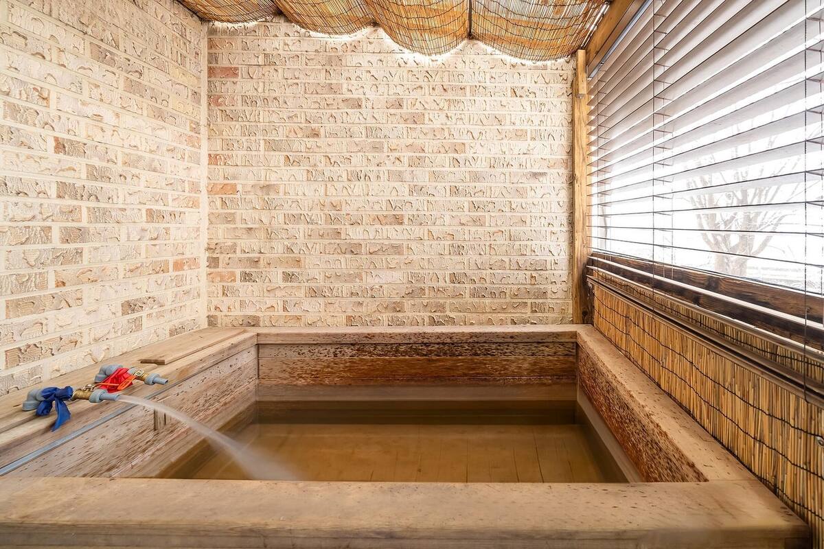 Ein traditionelles japanisches Onsen mit einem Steingrund-Bad, Bambusrollos und einer Backsteinwand.