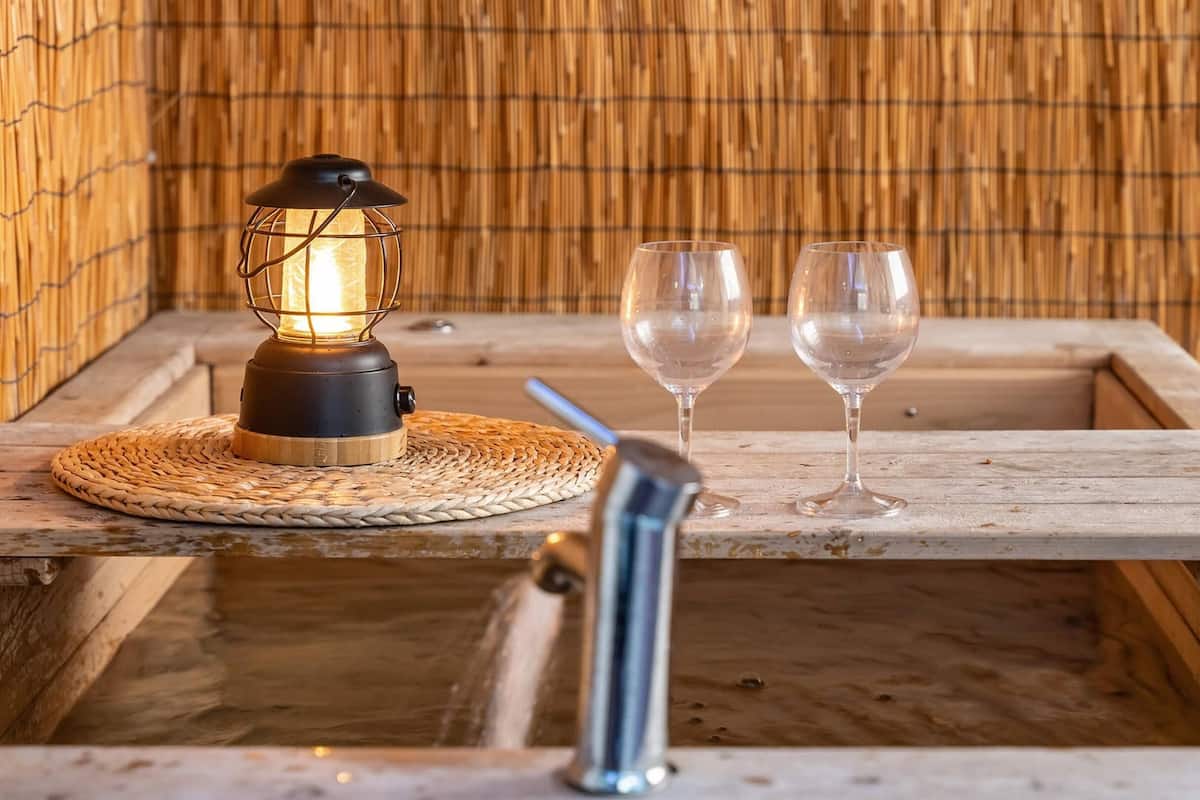 Eine Holz-Wohlfühlwanne mit einer gewobenen Matte, einem beleuchteten Laternen und zwei leeren Weingläsern.