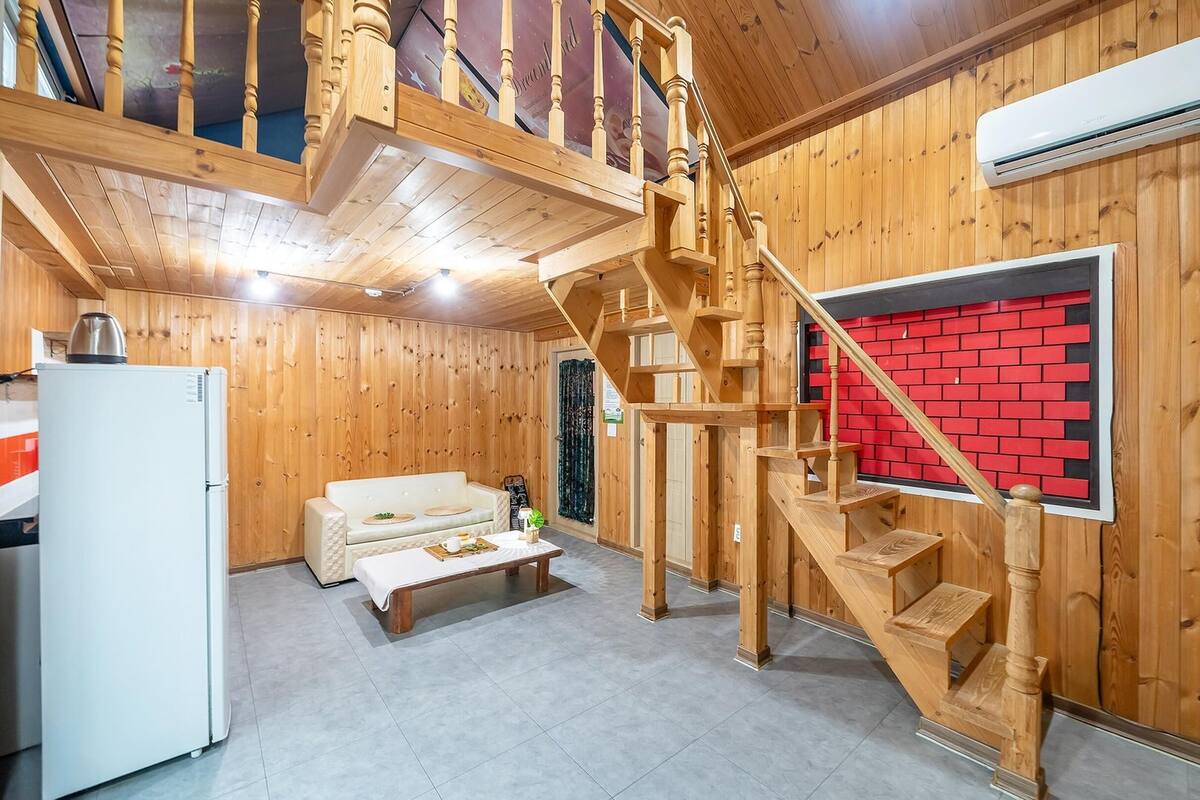 Ein Holzinnenraum mit Treppe, einem weißen Kühlschrank, einer Couch und einer roten Ziegelwand.